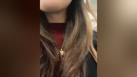 Media: Video of a woman's neck and shoulder, showing long, wavy brown hair, a burgundy top, and a gold necklace. The background is blurred, focusing on the details of her hair and jewelry.