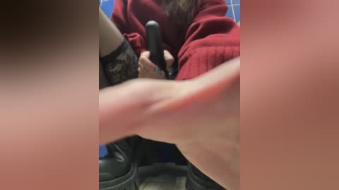 Media: Video of a person with fair skin wearing a red sweater, black lace stockings, and black shoes, with a black cane, sitting on a tiled floor.