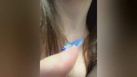 Media: Close-up video of a woman's head and neck, showing her pulling out a strand of brown hair with her right hand, revealing a blue shirt collar. The background is blurred, focusing on the intimate act.