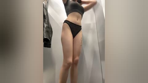 Media: A video of a woman in a dressing room, wearing a black sports bra and matching high-cut panties, standing with her back to the camera, partially obscured by a white curtain.