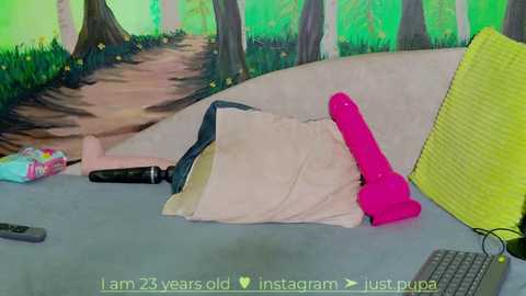 Media: A colorful video featuring a large, pink dildo on a bed, surrounded by a green forest mural, with a yellow pillow and laptop visible.