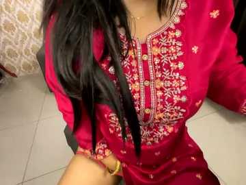 Media: Video of a woman with long black hair, wearing a vibrant red embroidered kurta with intricate floral patterns, seated on a white tiled floor.