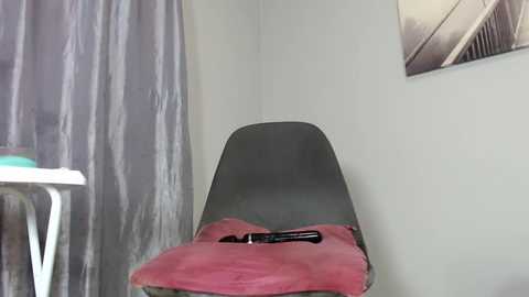 Media: Video of a modern, grey plastic chair with a pink cushion and a black pen on top. Background features a white wall, grey curtain, and a blurred desk.