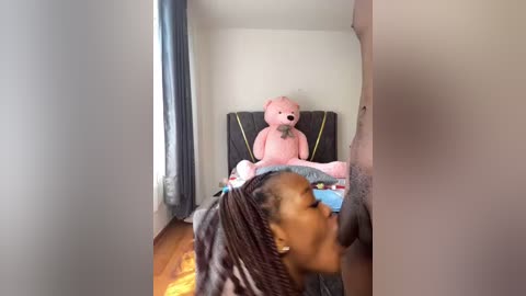 Media: A video of a young Black girl with braided hair, standing in a doorway, looking into a room with a pink teddy bear on a bed.