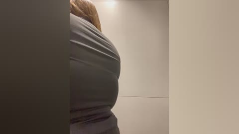 Media: Video of a person's back in a dark grey jacket, standing in a minimalist, beige-walled hallway with smooth, clean surfaces and a subtle ambient light.