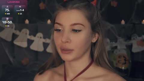 Media: Video of a young woman with fair skin, long blonde hair, wearing a red necklace and a devil horns headband. Background shows Halloween decorations.