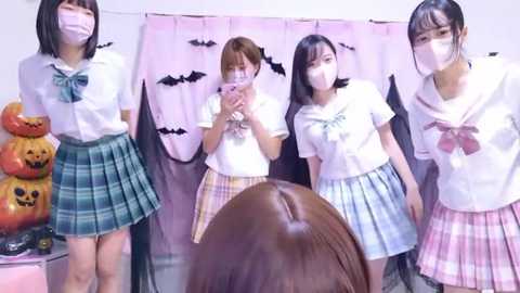 Media: Video of four Japanese schoolgirls in Halloween costumes, wearing masks, posing in front of a pink curtain with bats.