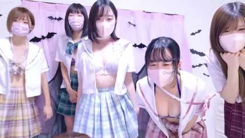 Media: Video of five Asian women in school uniforms with face masks, covering their mouths and noses, in a room with pastel pink curtains and bats.