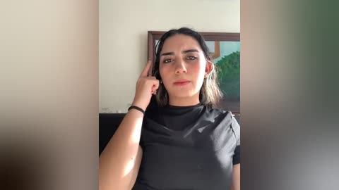 Media: Video of a young woman with medium skin tone, long dark hair, and a slim physique, wearing a black t-shirt, standing indoors near a window with greenery outside.