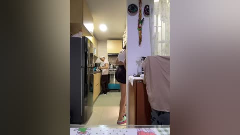 Media: Video of a small, cozy kitchen with a fridge, stove, and counter space. A person, partially visible, stands in the background. The walls are white, and the floor is tiled.