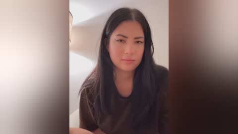 Media: Video of a young Asian woman with straight black hair and light skin, wearing a black shirt, sitting on a white staircase, with blurred, warm-toned vertical bars on either side.