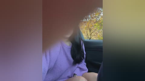 Media: A blurry video of a person with long, dark hair, wearing a lavender robe, sitting in a car with the window open, revealing autumn trees outside.