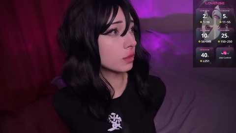 Media: Video of a young woman with pale skin and long black hair, wearing a black shirt with a white logo, looking contemplative against a red and purple backdrop.