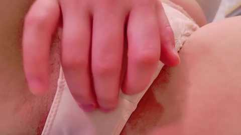 Media: A close-up video of a fair-skinned hand gently touching a woman's white lace underwear. The image focuses on the fingers and the delicate fabric, highlighting the soft textures and intimate setting.