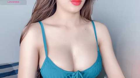 Media: Video of a light-skinned woman with long brown hair, wearing a turquoise tank top that accentuates her ample cleavage, set against a plain, white background.