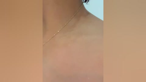 Media: A close-up video of a person's bare, light-skinned neck, showing a delicate gold chain necklace with a small pendant. The background is out of focus, featuring a soft, pastel blue hue.