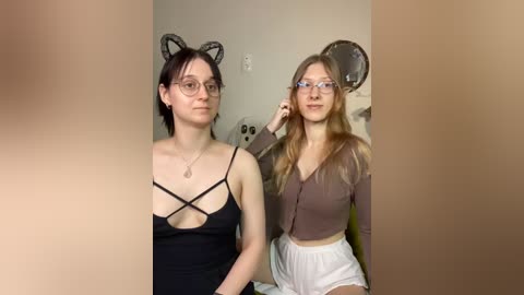 Media: Video of two young women with glasses, one in a black crisscross top, the other in a brown cardigan and white shorts.