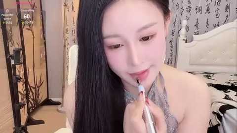 Media: Video of an Asian woman with long black hair, fair skin, and light makeup, using an electric toothbrush in a modern, white bedroom with patterned curtains.