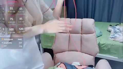 Media: Video of a medical examination with a young woman in a white dress and a large, pink, cushioned exam chair. The room has green curtains and a digital screen showing medical data.