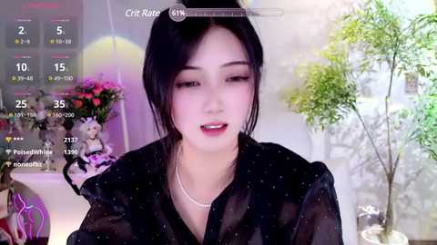 Media: Video of a young East Asian woman with fair skin, black hair, and red lipstick, wearing a black sheer top. Background features a green potted plant and a pink flower arrangement.