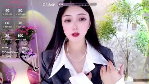 Media: Video of an Asian woman with long black hair, fair skin, and red lipstick, wearing a white blouse and black blazer, holding a card. Background includes a potted plant and a pink vase.