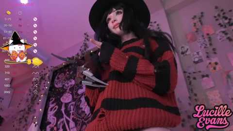 Media: Video of a pale-skinned woman with long black hair, wearing a black witch hat and a red striped sweater, holding a framed photo, in a purple-lit room with Halloween decorations.