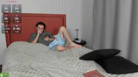 Media: Video of a man in a green shirt and blue shorts lying on a gray bed, looking at a smartphone, surrounded by digital health metrics and pillows.