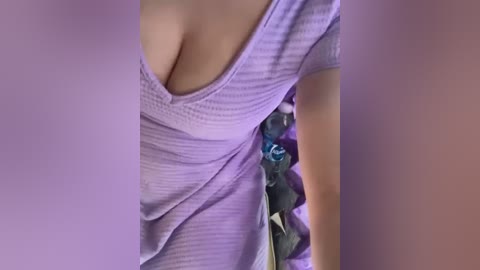 Media: Video of a woman's cleavage, wearing a purple striped top with a deep neckline, revealing ample cleavage. Her right arm is bent, holding a purple flower. The background is blurred, creating a focus on her chest area.