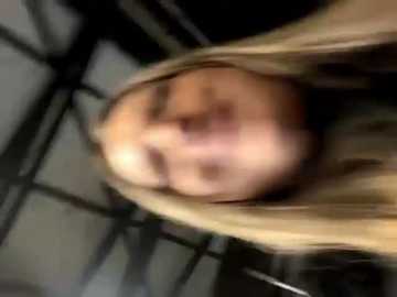 Media: A blurry video shows a close-up of a person's face with blonde hair, wearing a black shirt, against a dimly lit, metal-framed background.