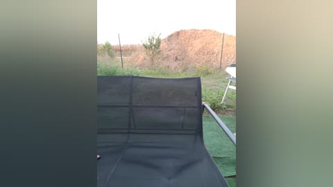 Media: Video of a black mesh camping chair with a view of a grassy hillside under a clear sky. The foreground is slightly blurry, emphasizing the chair and the open space beyond.