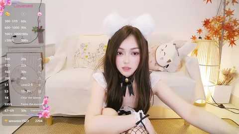 Media: Video of an Asian woman in a white maid outfit, sitting on the floor in a cozy living room with autumn-themed decorations.