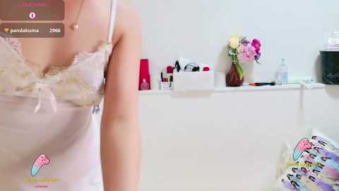 Media: A video of a woman wearing a lacy white camisole, with a blurred background featuring makeup items and a floral arrangement.