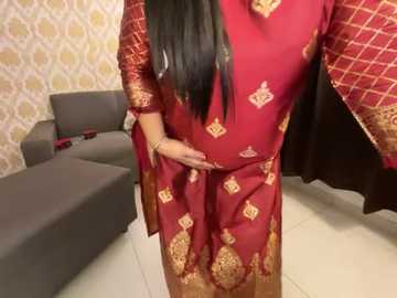 Media: A video shows a woman in a red embroidered kurta, with long black hair, standing indoors. The background features a gray couch, patterned wallpaper, and a partially open closet.