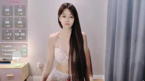 Media: Video of an East Asian woman with long, straight black hair, wearing a white lace bra and panties, standing in a minimalist bedroom with a digital clock displaying 2:20 AM, and a light blue curtain in the background.