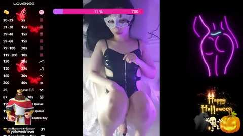 Media: Video of a slender, light-skinned woman in black latex lingerie lying on a bed, with a glowing neon \"Happy Halloween\" sign and a \"Love Level\" bar.