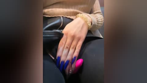 Media: Video of a person's hands with long, blue and pink acrylic nails, wearing a beige sweater and black leather pants.