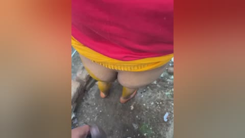 Media: A video of a person's buttocks in bright red shorts with yellow trim, standing on a dirt path with a blurry, red-tinted background.