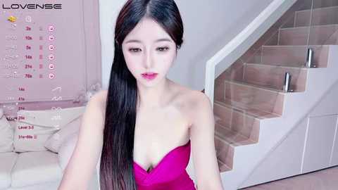 Media: A video of a young East Asian woman with long, straight black hair, wearing a strapless pink dress, sitting on a modern white staircase.