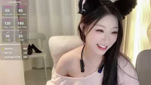 Media: A young Asian woman with long black hair and black cat ears, wearing a light off-shoulder top, sits indoors. Background includes a white chair, a window, and a digital live stream overlay with statistics.