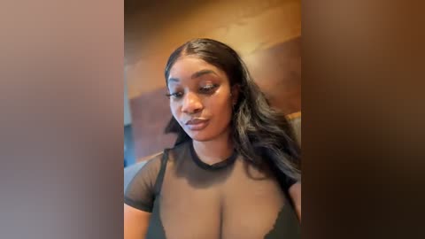 Media: A video of a confident Black woman with a medium complexion, wearing a sheer black top revealing her ample cleavage. Her long, wavy black hair cascades over her shoulders.