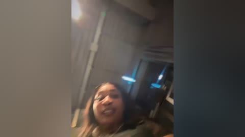 Media: A blurry video shows a young woman with light skin, smiling, wearing a headset, in a dimly lit room with a white ceiling and a door in the background.