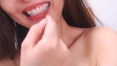 Media: Video of a smiling, light-skinned woman with straight, brown hair, showing braces and a playful expression. She is bare-shouldered, with a subtle background of white.