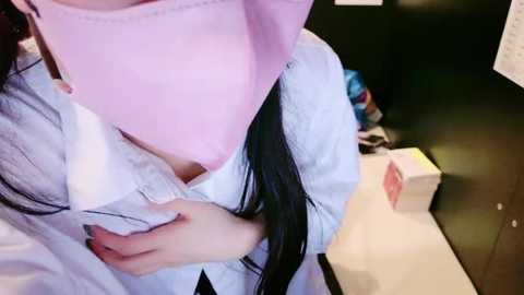 Media: Video of a person wearing a pink mask, white robe, and white gloves, holding a white tissue box in a dimly lit room with a black background.