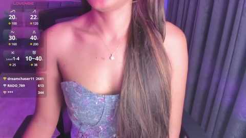 Media: A video of a young woman with long, straight, dark brown hair, wearing a strapless, glittery blue dress, against a purple-lit backdrop with a smartphone screen displaying live stream details.