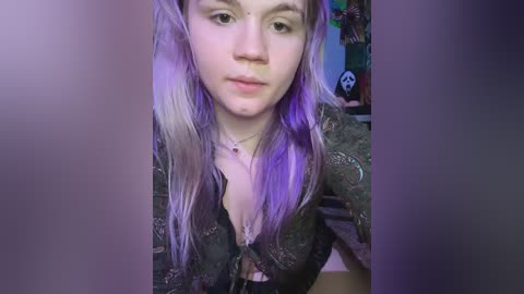 Media: Video of a pale-skinned, young woman with long, vibrant purple and white hair, wearing a black lace top with a plunging neckline, in a dimly lit room with a skull decal on the wall.