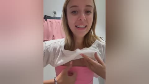 Media: A candid video of a young woman with fair skin, straight blonde hair, and a white long-sleeve shirt, lifting it to reveal her breasts.