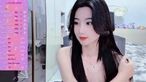 Media: Video of a young East Asian woman with long black hair, pale skin, and small breasts, wearing a necklace, in a modern bedroom with white walls and soft furnishings.