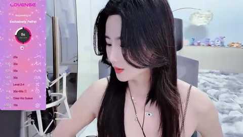 Media: Video of a slender, fair-skinned Asian woman with long black hair, wearing a black strapless top, sitting in a soft light room. Left side shows a \"Live\" screen with camera controls.