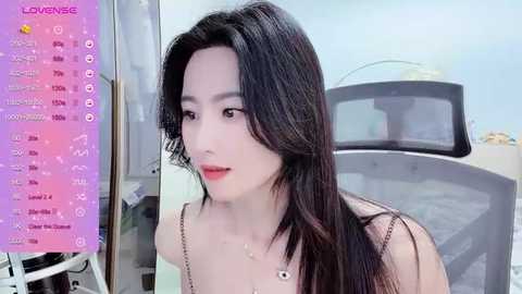 Media: Video of a fair-skinned, East Asian woman with long black hair, wearing a black spaghetti-strap top, looking contemplative. Background includes a car and a pink calendar with icons.