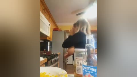 Media: A blurry video of a woman with blonde hair, wearing a black top, baking in a cozy kitchen with wooden cabinets, stainless steel appliances, and a \"Sugar in the Raw\" bottle on the counter.